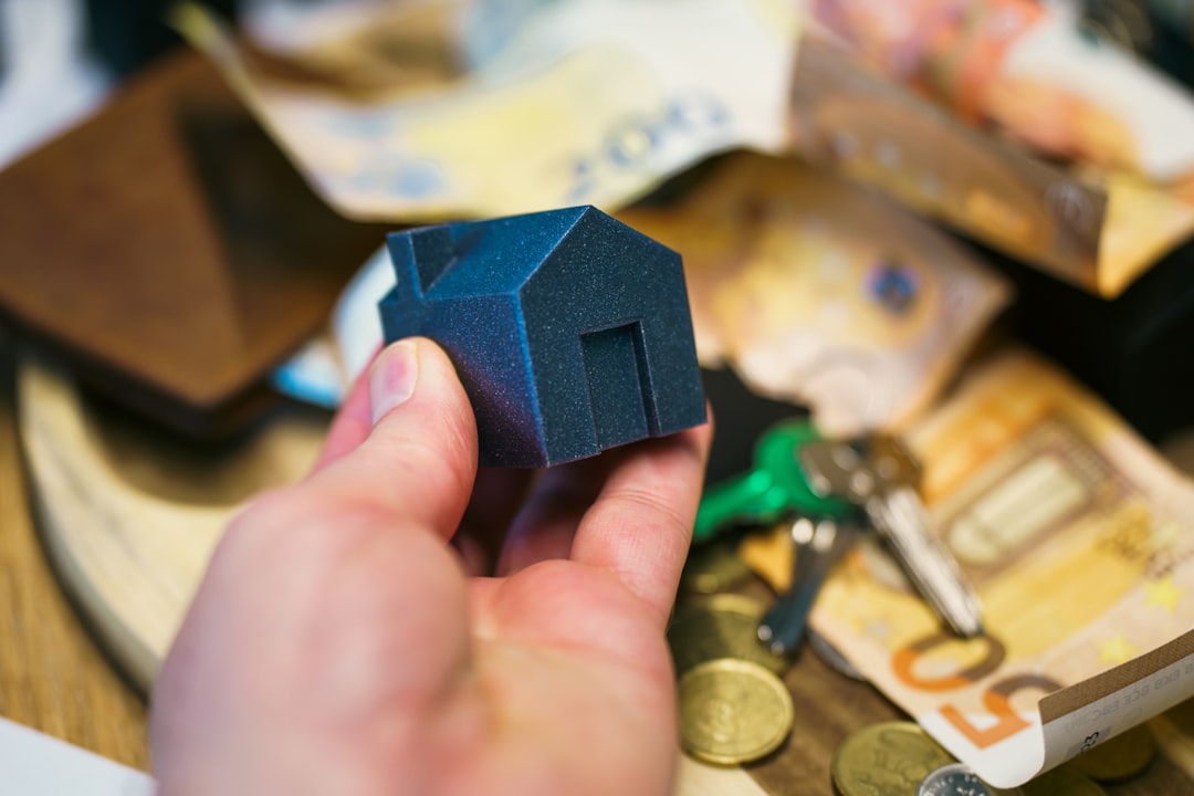 A close-up of a person's hands using a magnifying glass to carefully review legal documents next to a small model of a house, representing navigating complex rental regulations.