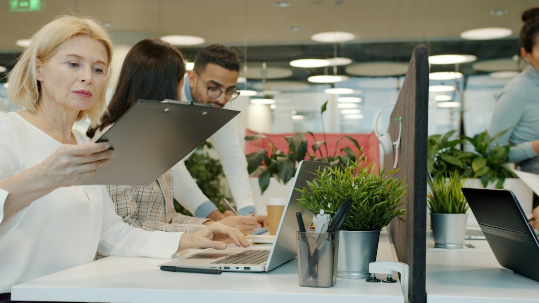 Group of professionals in a bright, modern office attentively reviewing architectural blueprints spread across a table, sy...
